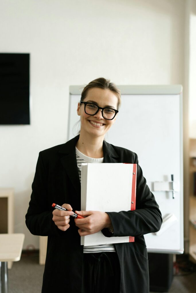 Professional woman in a classroom holding documents and smiling warmly.