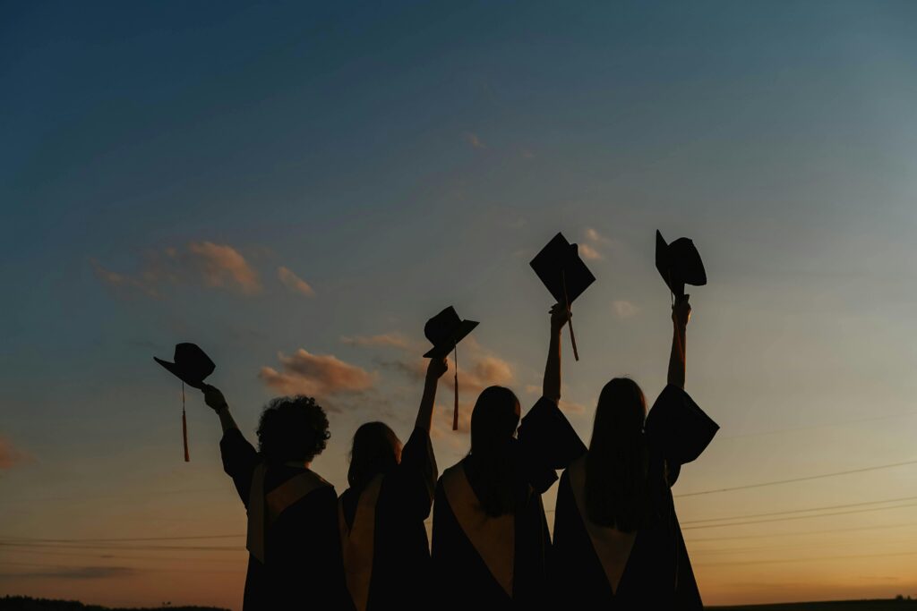 A group of graduates celebrate by raising their caps against a vibrant sunset sky, symbolizing achievement.
